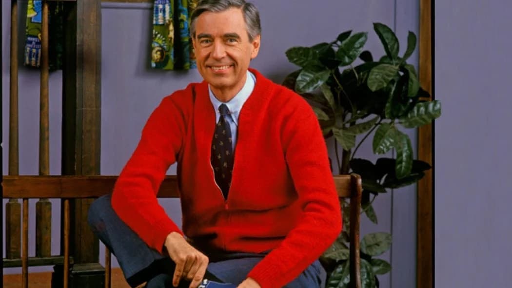 Fred Rogers seated in a red cardigan.